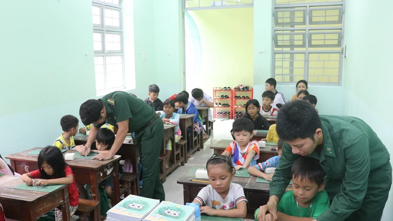 绿衣老师们耐心地引导孩子们书写每一笔每一画。图自越通社